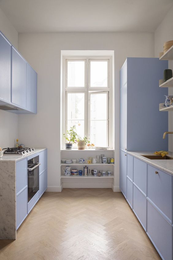 a pretty periwinkle galley kitchen with white stone countertops and open shelving and built-in tea set shelves