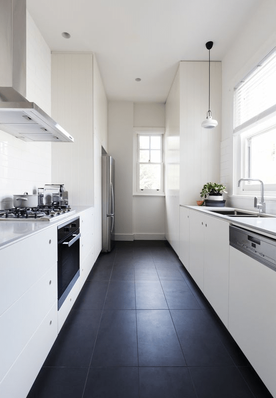 a minimalist gallery kitchen in black and white with tiled floors, elegant white kitchens, sufficient natural light and pendant lamps