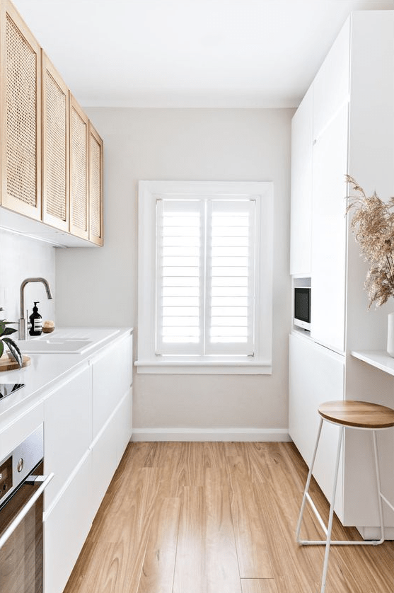 a minimalist white galley kitchen with elegant cabinets, rattan upper cabinets, a wooden stool and some grass