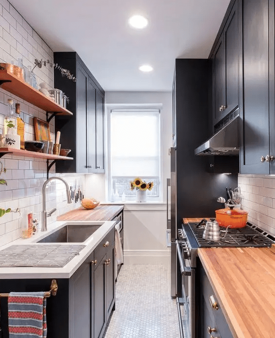 a navy galley kitchen with shaker cabinets, butcher block countertops, open shelving and some built-in lights