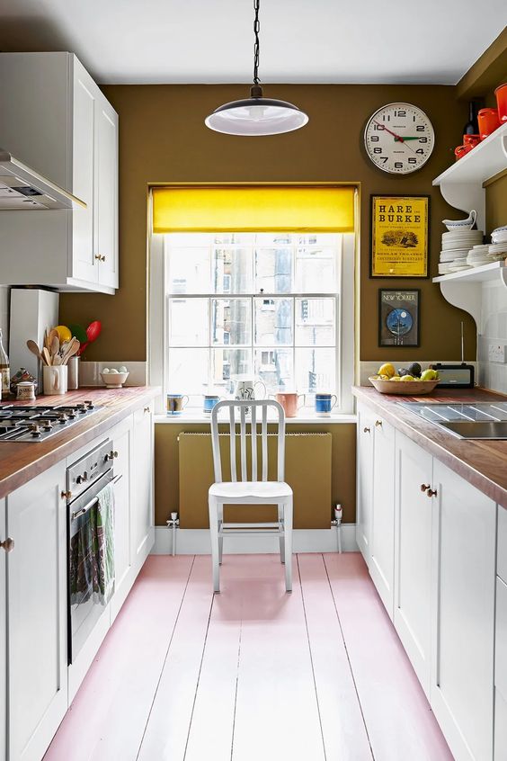 a pretty galley kitchen with mustard walls, white cabinets, butcher block countertops and a pink floor, a hanging lamp
