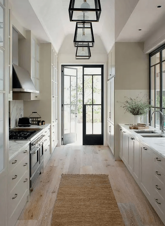 A sophisticated white farmhouse kitchen features a shaker cabinet, black handles, a vintage-style stove and hood, and framed hanging lamps