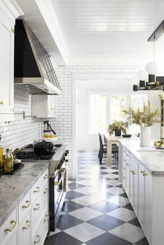 a white farmhouse kitchen with shaker cabinets, stone countertops, black and white tiles, a vintage-style range hood, and cool lamps