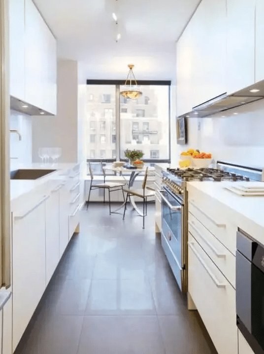 a white galley kitchen with sleek cabinetry, built-in lights and appliances, and a window dining area