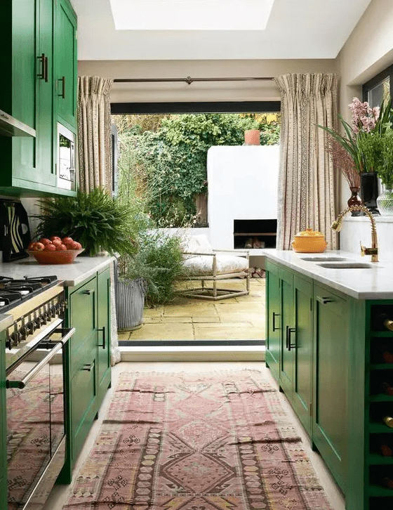 an emerald green galley kitchen with shaker cabinets, white stone countertops, a statement boho rug, and an entryway to the patio