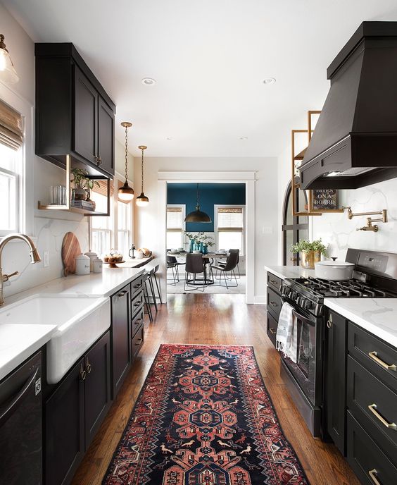 a chic black galley kitchen with white countertops and brass accents, as well as a printed rug and vintage pendant lamps