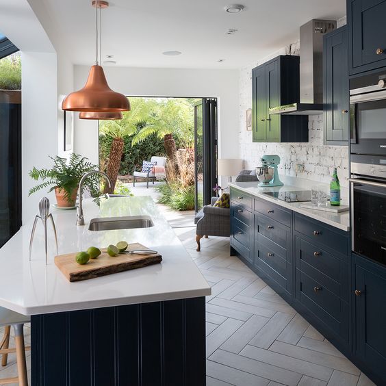 a stylish galley kitchen with navy blue cabinets and white stone countertops, copper pendant lamps and a brick backsplash
