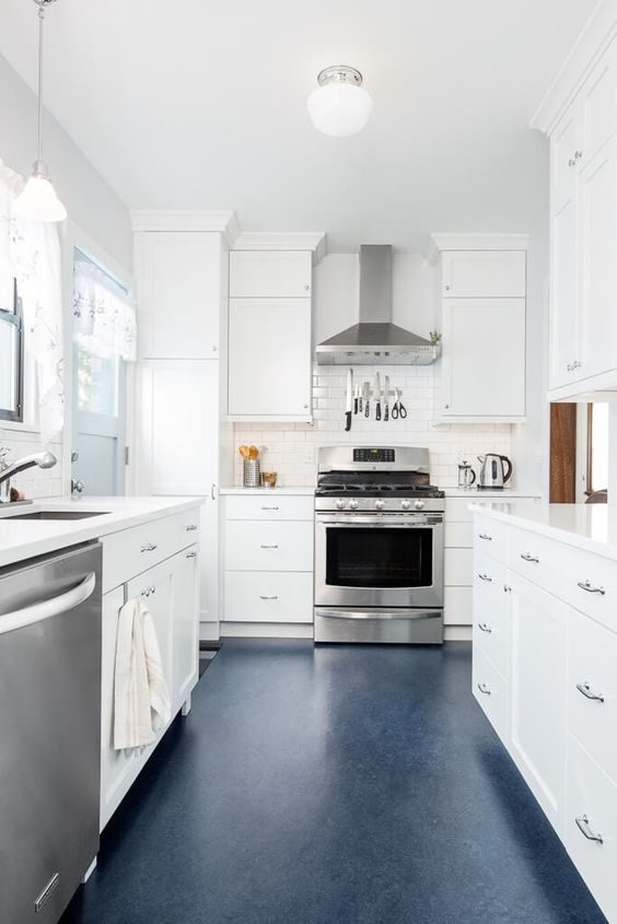 a calm, neutral galley kitchen with white cabinets and countertops, a navy floor, and stainless steel appliances