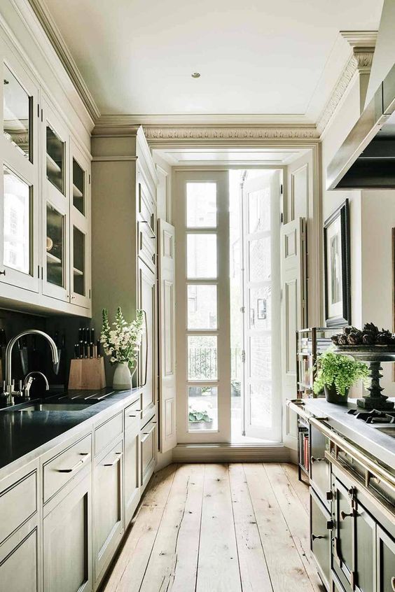 a traditional galley kitchen with dark vintage cabinets, a wooden floor and access to the balcony with lots of natural light