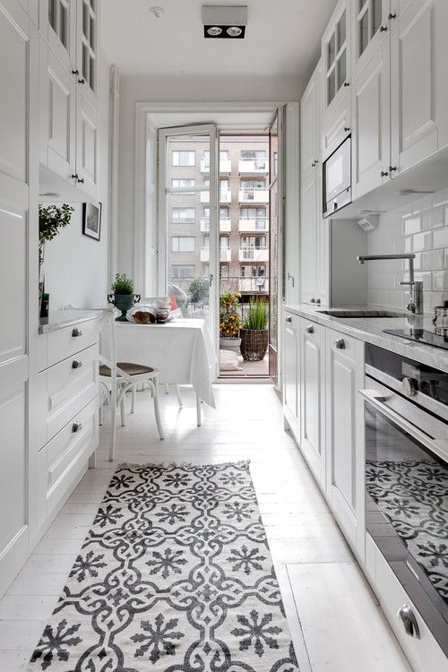 an airy white Scandinavian kitchen with white cabinets, a small balcony dining area and a printed rug