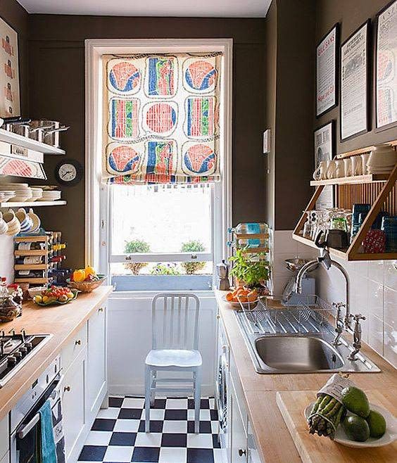 an eclectic galley kitchen with black walls, checkered flooring, white cabinets with butcher block countertops and a colorful curtain