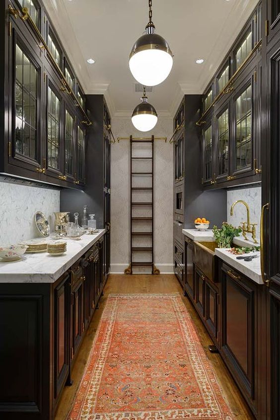 a sleek dark kitchen with traditional dark cabinets, a ladder to get things out of upper cabinets, and neutral stone countertops