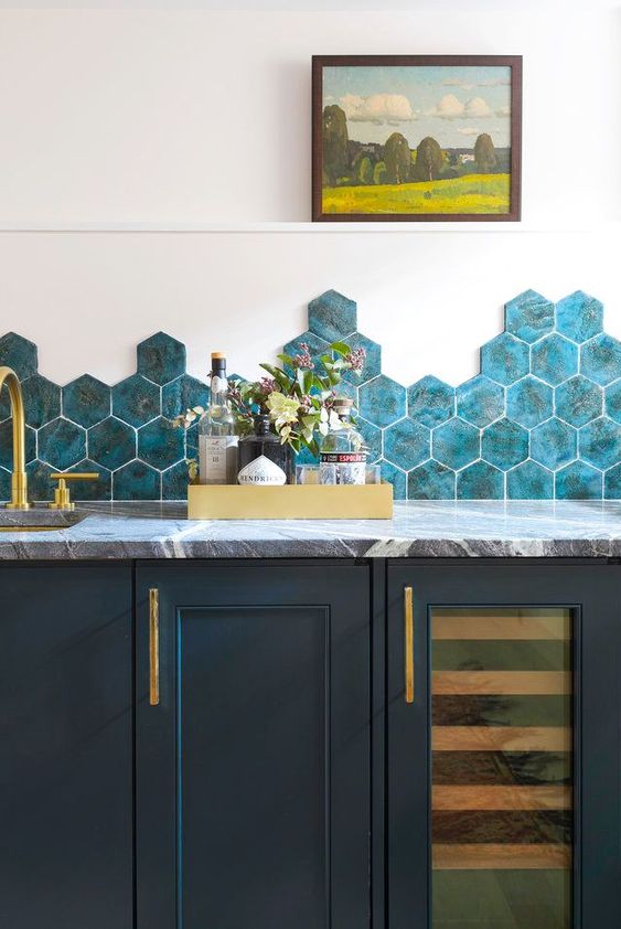 A striking navy blue kitchen with gray marble countertops and striking blue hexagon tiles and gold fixtures is enchanting