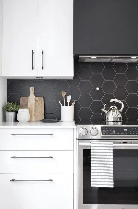 A modern kitchen with white cabinets, a black matte hexagonal tile backsplash and a black extractor hood looks rich in contrast