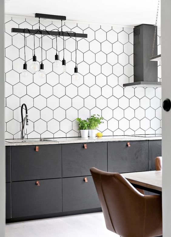 A graphite gray Scandinavian kitchen with an extended backsplash made of hexagonal tiles, pendant lamps and leather handles