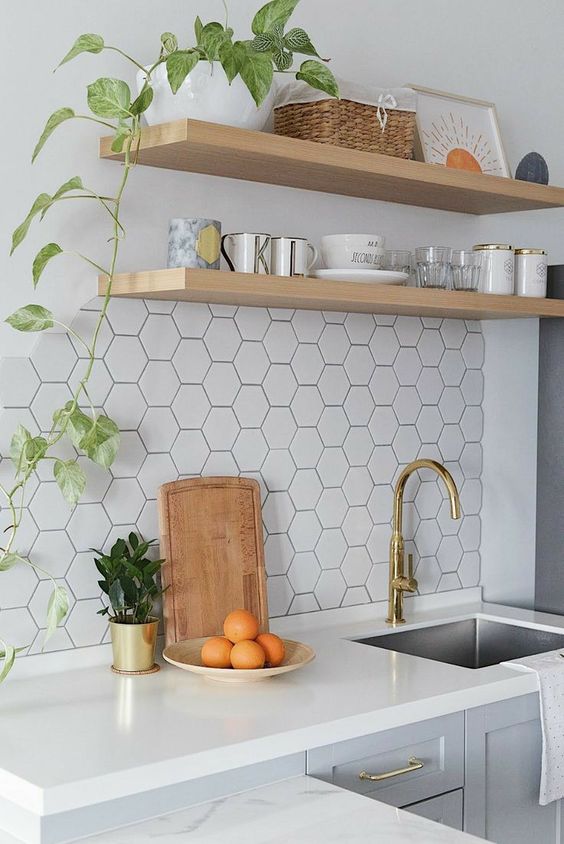 A light gray kitchen with white stone countertops, open shelving, a white hexagonal tile backsplash and lots of greenery
