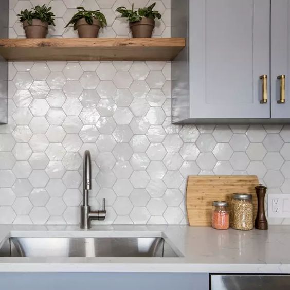 A gray kitchen with white stone worktops and a glossy white hexagonal tile backsplash and stained shelves