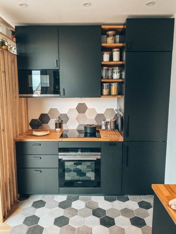 A matte black kitchen with butcher block countertops, open shelving and hexagonal tiles in gray, tan and beige on the walls and floor