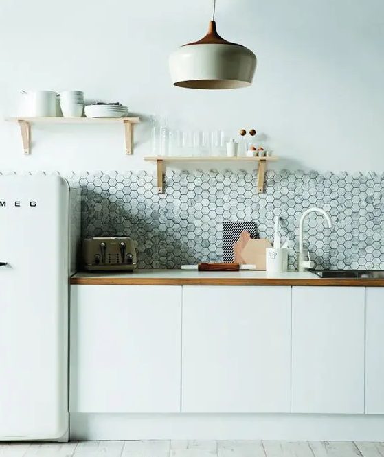 A minimalist white kitchen with wooden elements and a gray marble tile backsplash with hexagon tiles