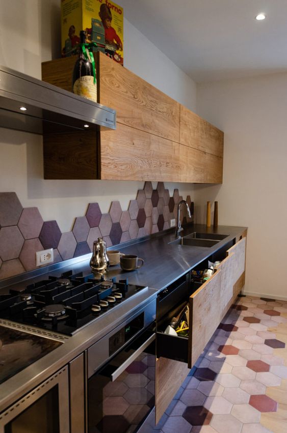 A modern stained kitchen with metal worktops and a splashback and floor of hexagonal tiles in bold pink and burgundy