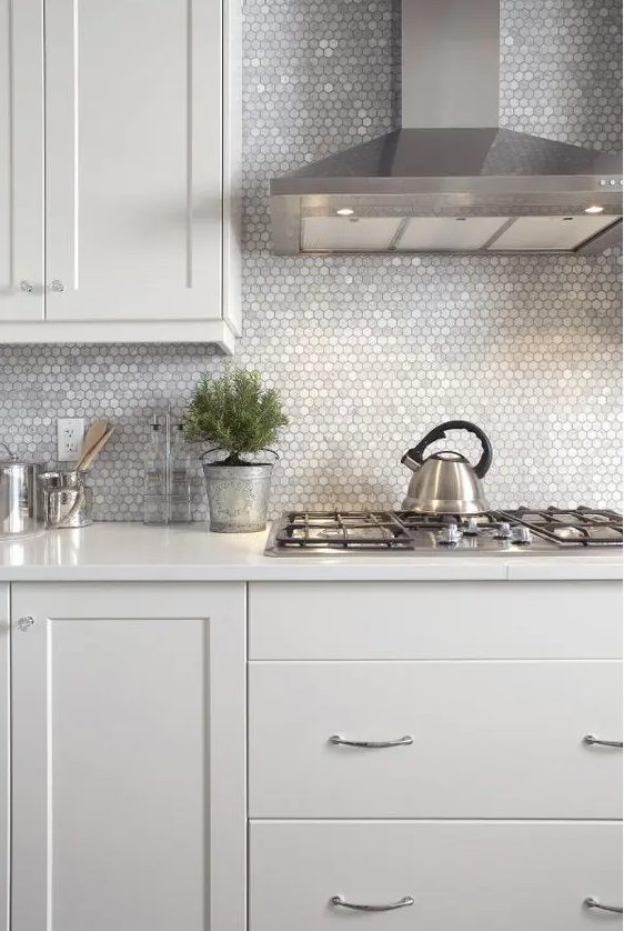 A neutral kitchen with a pretty silver backsplash made of small hexagonal tiles and stainless steel appliances that create a cohesive look