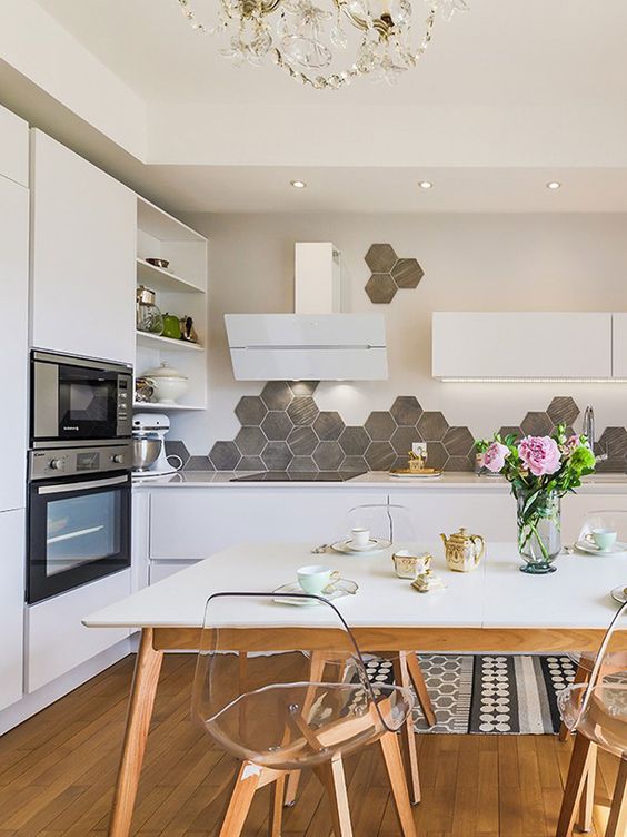 a Scandinavian eat-in kitchen with sleek white cabinets, a gray hexagon tile backsplash, built-in lights and a dining set