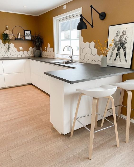 a Scandinavian kitchen with terracotta walls, white sleek cabinets, concrete countertops and a striking hexagonal tile backsplash