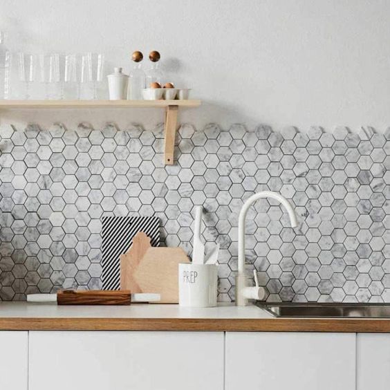 A sleek white kitchen with a gray marble hexagon tile backsplash, open shelving and white fixtures is beautiful