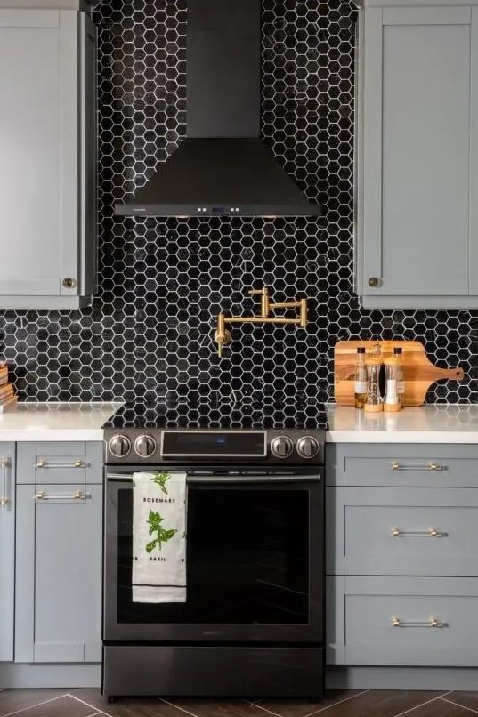A stylish gray farmhouse kitchen with white worktops and a back wall made of black hexagonal tiles as well as a black extractor hood looks very elegant