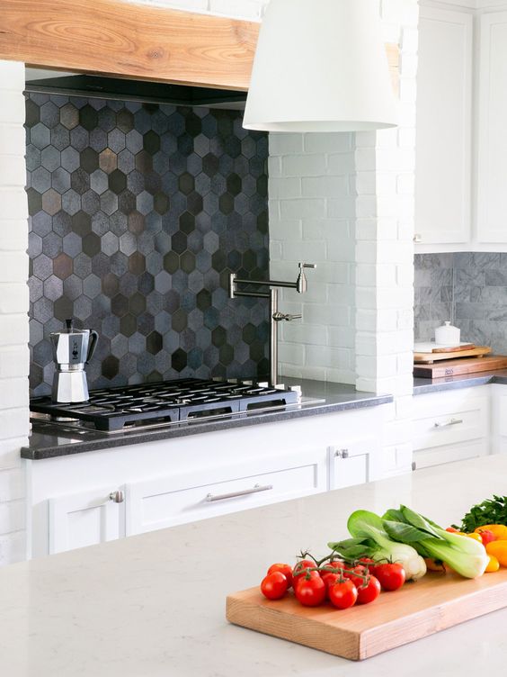 A white kitchen with a dark hexagon tile backsplash and gray countertops and gray marble tiles is cool