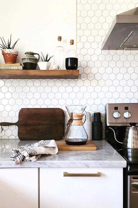a white Nordic kitchen with white countertops and a white hexagonal tile backsplash as well as open shelving and stainless steel appliances