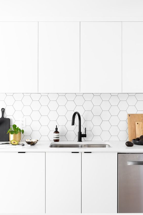 a white Scandinavian kitchen with elegant cabinets, a white hexagonal tile backsplash with black grout and black fixtures