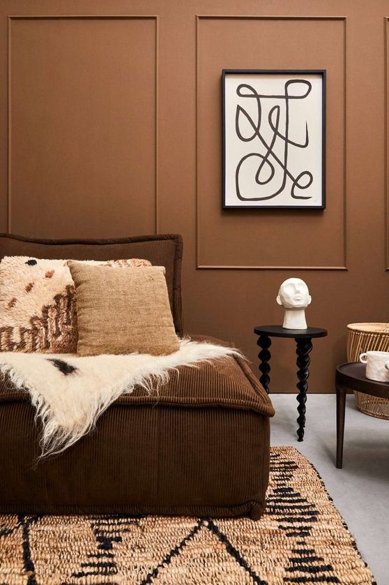 a modern living room with light brown walls, a brown sofa with cushions, tables and printed textiles
