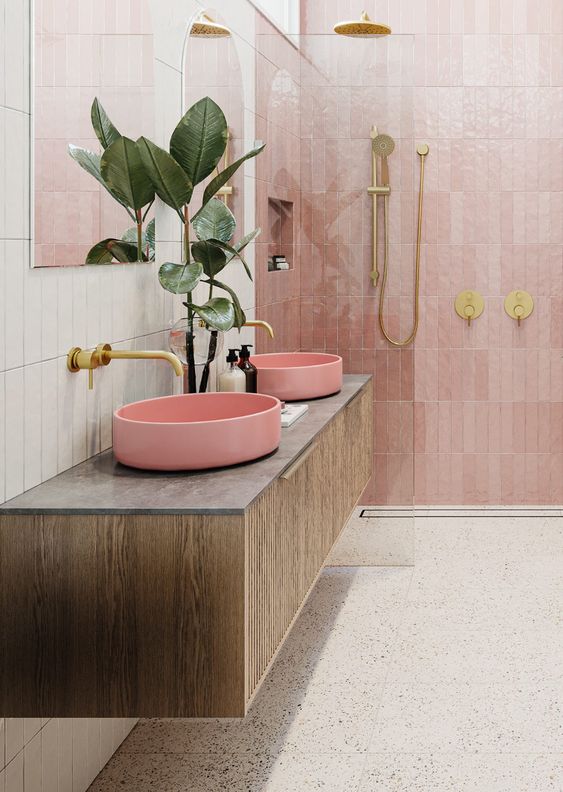 a beautiful modern bathroom with white stacked tiles and pink zellige tiles in the shower, a gray terrazzo floor, a stained vanity with a pink sink and gold hardware
