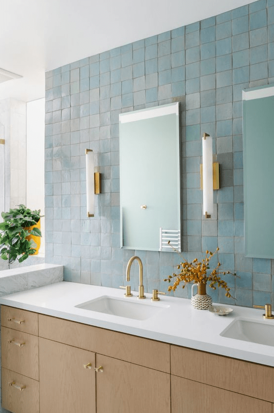 a gorgeous bathroom with blue zellige tiles, a light stained vanity, mirrors and sconces, and gold fixtures