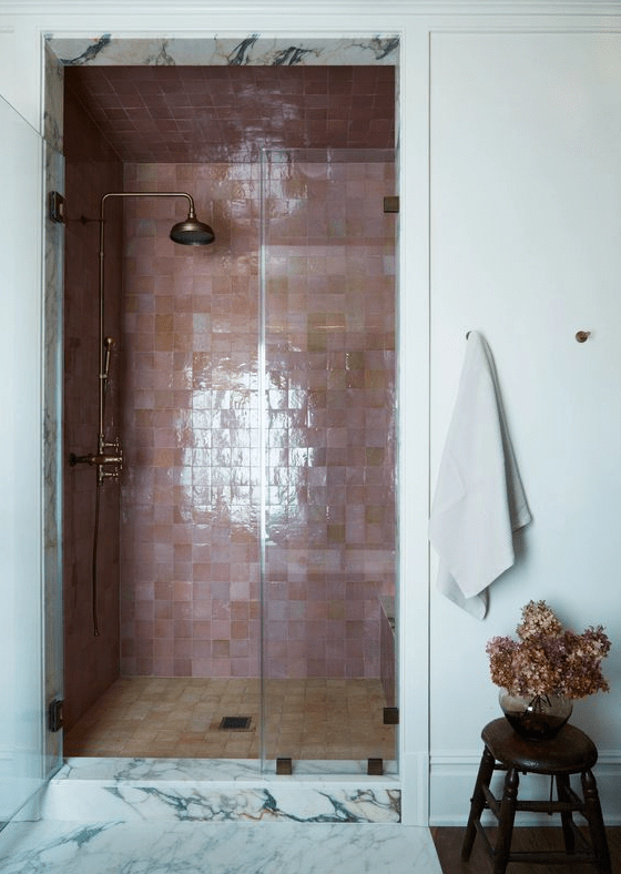 a bathroom with a shower area clad in pink and brown zellige tiles, brass fixtures and some flowers in a vase