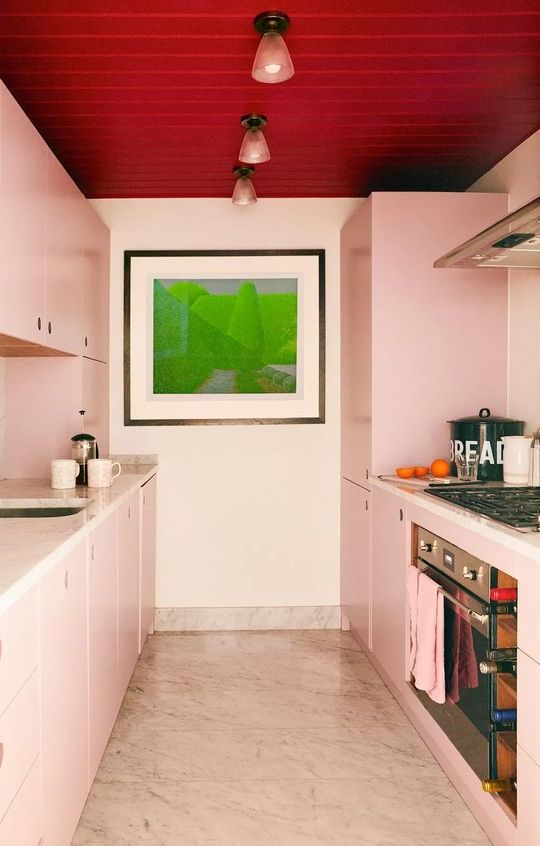 A blush galley kitchen with a red ceiling, white countertops, and a statement piece of art is a cool and unusual space